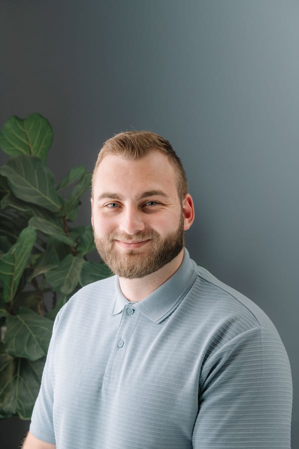 Jonge man met baard in een lichtblauwe polo, voor een grijsgroene wand met een vijgenboom
