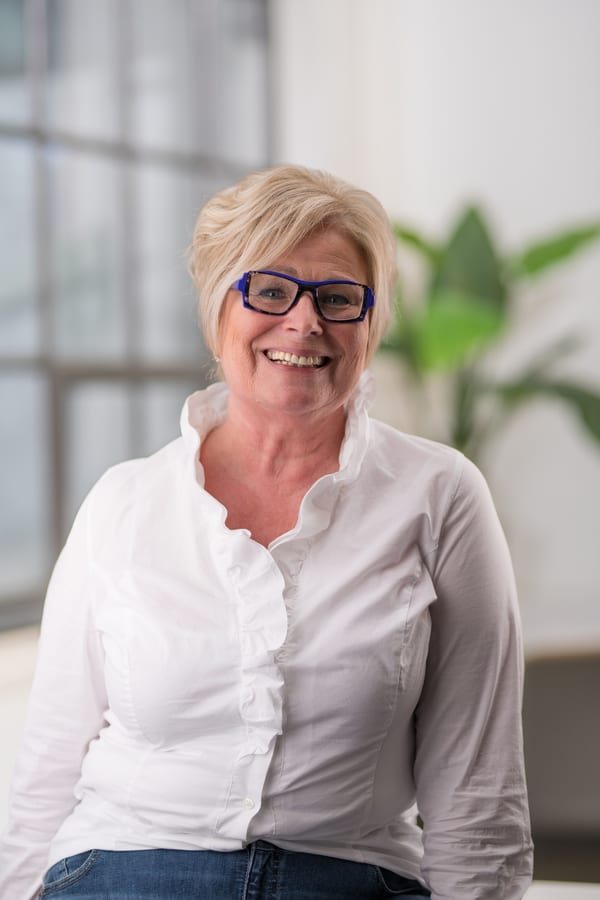 Vrouw met blauwe bril in een wit overhemd met ruches