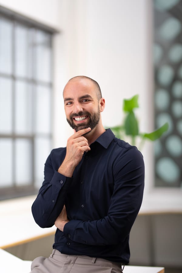 Man met baard in een donkerblauw overhemd, hand bij de kin
