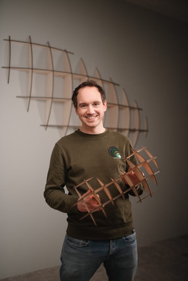 Man in een olijfgroene sweater die een houten wandobject vasthoudt